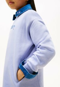 Lyslilla sweatshirt med en denimkrave, prydet med broderede blomsterdetaljer. Ærmerne er i denim, med et lille logo på ærmet.