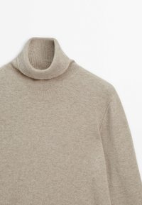 Pull à col roulé beige clair avec texture en maille fine, manches longues et col côtelé plié sur un fond blanc.