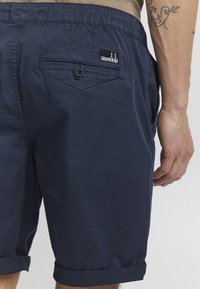 Shorts bleu marine en tissu léger, dotés d'une poche arrière boutonnée et d'une ceinture élastique avec un détail de revers.