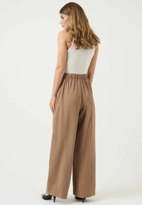 Lichtbruine wijde broek met een elastische taille, gemaakt van een soepele stof, gecombineerd met een witte mouwloze top. Luchtig en ontspannen pasvorm.