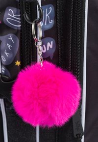 Portachiavi a pompon in pelliccia sintetica rosa dalla forma rotonda, appeso a un anello in metallo argento, attaccato a una cerniera nera di uno zaino.