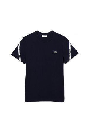 T-shirt bleu marine à manches courtes avec des rayures blanches du logo Lacoste sur les manches et un petit logo crocodile vert sur la poitrine gauche.