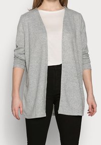 Cárdigan gris de frente abierto hecho de un material suave y Texturizado. Mangas largas con puños doblados, usado sobre una camisa de color claro y pantalones negros.