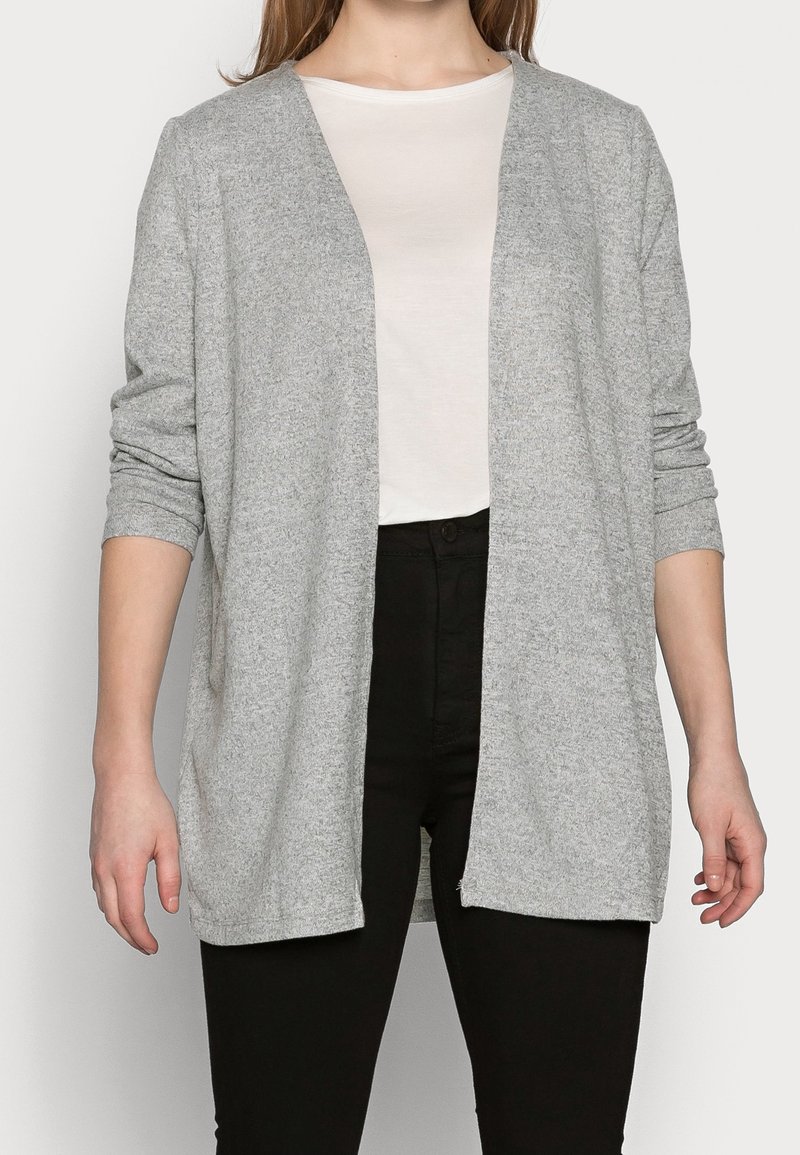 Cárdigan gris de frente abierto hecho de un material suave y Texturizado. Mangas largas con puños doblados, usado sobre una camisa de color claro y pantalones negros.