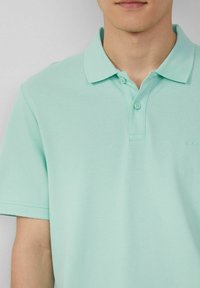 Mintgrünes Poloshirt mit klassischem Kragen, zwei Knöpfen und strukturiertem Stoff. Minimalistisches Branding auf der Brust.