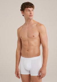 Bílé bavlněné boxerky s těsným střihem, s hladkým pasem a předním kapsičkovým prostorem. Model stojí na neutrálním pozadí a mírně se otáčí doleva.