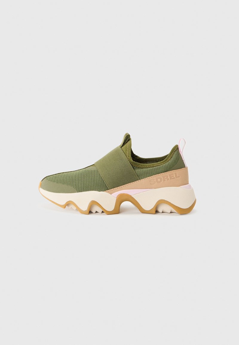 Grüne Sport Schuhe mit einem Mesh-Obermaterial, elastischem Riemen, pinken Akzenten und einer strukturierten, gewellten weißen und braunen Sohle.
