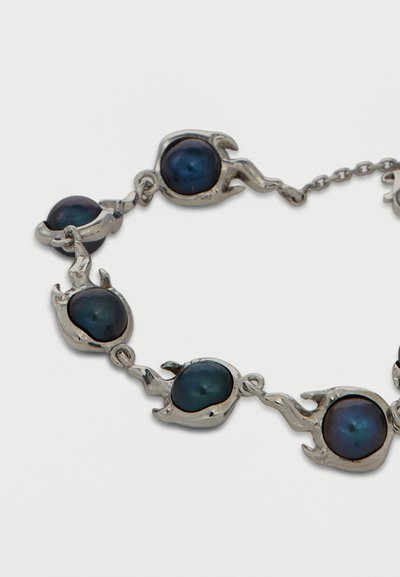 Ασημένιο βραχιόλι με συνδεδεμένες φλόγες που κρατούν στρογγυλές σκούρες μπλε πέρλες σε λευκό φόντο.