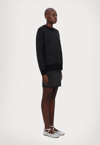 Pull en tricot noir avec un motif à pois blancs, associé à une jupe assortie. Le modèle porte des ballerines en argent avec des brides autour de la cheville.