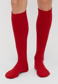 Skarpetki do kolan w kolorze czerwonym, wykonane z teksturowanej dzianiny, z prążkowanym ściągaczem u góry i wzorem w jodełkę na całej długości cholewki.
