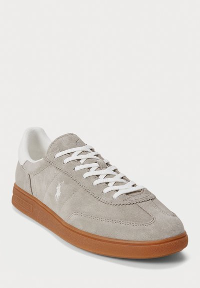 Sneaker in suede grigio con dettagli e lacci bianchi. Presenta una suola in gomma con un design testurizzato e un piccolo logo sul lato.