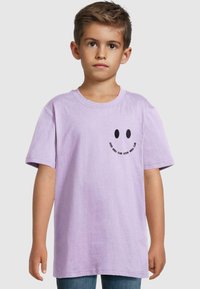 Lillā krāsas kokvilnas T-krekls ar īsām piedurknēm, kurā kreisajā krūtīs ir melna smiley sejiņa un uzraksts "GOOD VIBES CLUB".