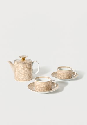 Porcelæns tekande og to matchende tekopper med underkopper, med beige blomsterdekorationer og et låg med guldfarvet tone på tekanden.