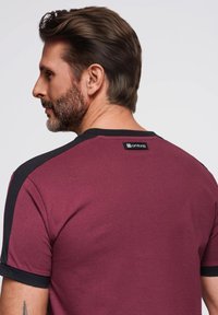 Vínová tričko s černými akcenty na ramene, krátkými rukávy a kulatým výstřihem. Na zadní části krku se nachází štítek. Materiál: bavlna.
