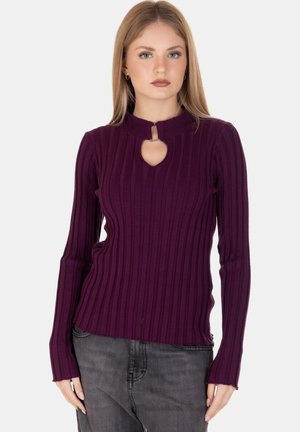 Maglietta lunga a maniche con righe viola, dettagli con scollatura a chiave, tessuto testurizzato e design aderente, abbinata a jeans scuri.