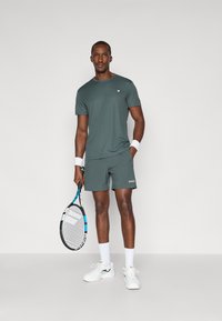 Roheline spordipolt ja lühikesed püksid, pehme kangas, lühikesed varrukad, ümar kaelus, koos tennisereketi, randmepaelte ja spordijalatsitega.