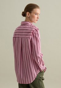 Langsleeve shirt in roze stof met zwarte verticale strepen en een button-down kraag; heeft een rugpand en een relaxte pasvorm.