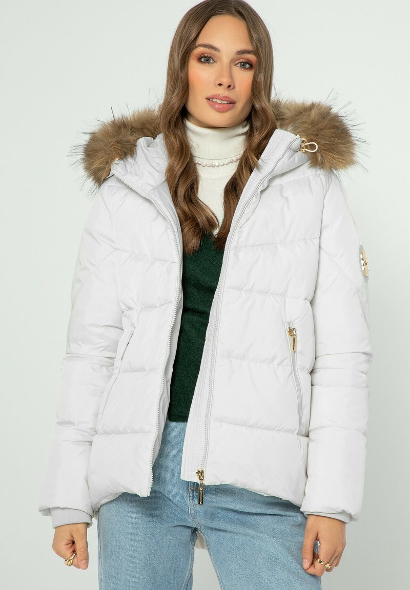 Přefoukaná bunda světle šedé barvy s odnímatelnou kapucí s kožešinovým lemem, kapsami na zip a zlatými kovovými detaily. Vyznačuje se prošívanou texturou.