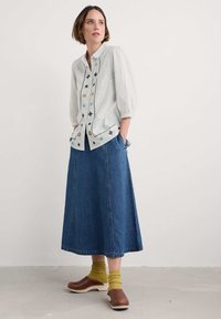 Camisa de botones de manga larga de color claro con detalles de bordado, combinada con una falda de denim, calcetas amarillas y zuecos de tacón de madera.