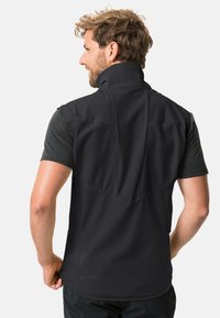 Gilet nero senza maniche con colletto alto, texture liscia e design del pannello posteriore. Include tasche laterali e logo del marchio sull'orlo.