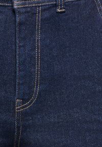 Tamsiai mėlynos spalvos džinsinio audinio medžiaga su matomomis oranžinėmis siūlėmis ir arti pažvelgus į priekinės kišenės ir liemens siūlės siūles.