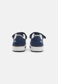 Blå ruskinds sneakers med hvide detaljer, der har et lavprofil design og velcrostropper. Rund tå og tekstureret ydersål for bedre greb.