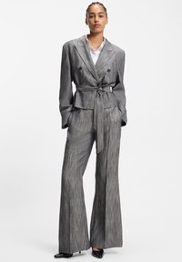 Szürke csíkos, testre szabott öltöny övvel átkötve, bő szárú nadrággal és kétsoros blézerrel, amely klasszikus gallérral és zsebekkel rendelkezik.