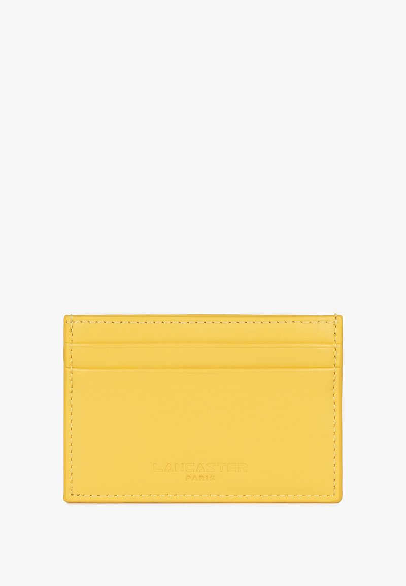 Porte-cartes en cuir jaune avec plusieurs fentes pour cartes, coutures visibles et logo de la marque embossé en bas. Texture lisse.