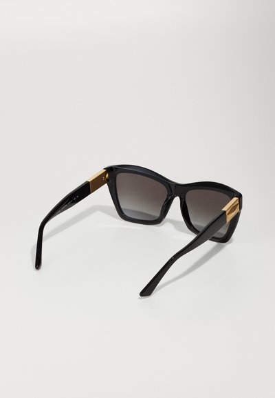 Lunettes de soleil noires avec une finition brillante, monture carrée, verres dégradés et accents en or sur les branches. Design rectangulaire et élégant.