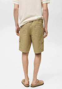 Pantaloni cargo verde oliva in tessuto leggero con tasche a pattina, un taglio rilassato e una tasca posteriore discreta. Abbinati a un top color crema.