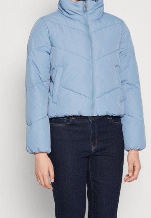 Lyseblå dunjakke med høj krave, lynlås foran, sidelommer og elastiske manchetter, båret med mørkeblå jeans.