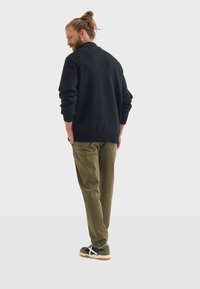 Schwarzer Strickpullover mit Rundhalsausschnitt, olivgrüne Hose und schwarze Sneakers mit weißen Akzenten, von hinten betrachtet.