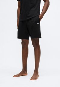 Μαύρα σορτς από μαλακό ύφασμα, με ελαστική μέση και πλαϊνές τσέπες, με λευκό λογότυπο "BOSS" στο αριστερό πόδι.