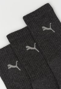 Tres pares de calcetines gris oscuro con textura acanalada, que presentan un pequeño diseño de logo gris claro en el lateral de cada calcetín.