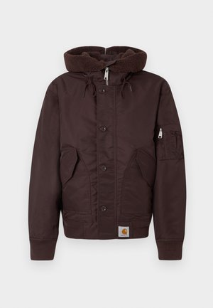 Brūns polsterēts jaka ar biezu, teksturētu kapuci, priekšējiem pogām, sānu kabatām un piedurknes kabatu. Iezīmē ribotas piedurknes un apakšmalu.