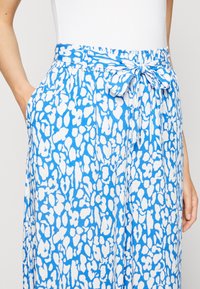 Blauw-witte rok met patroon en een tailleband met striksluiting, gemaakt van een lichte, gladde stof met zijzakken. Het ontwerp heeft een vloeiende, sierlijke vorm.