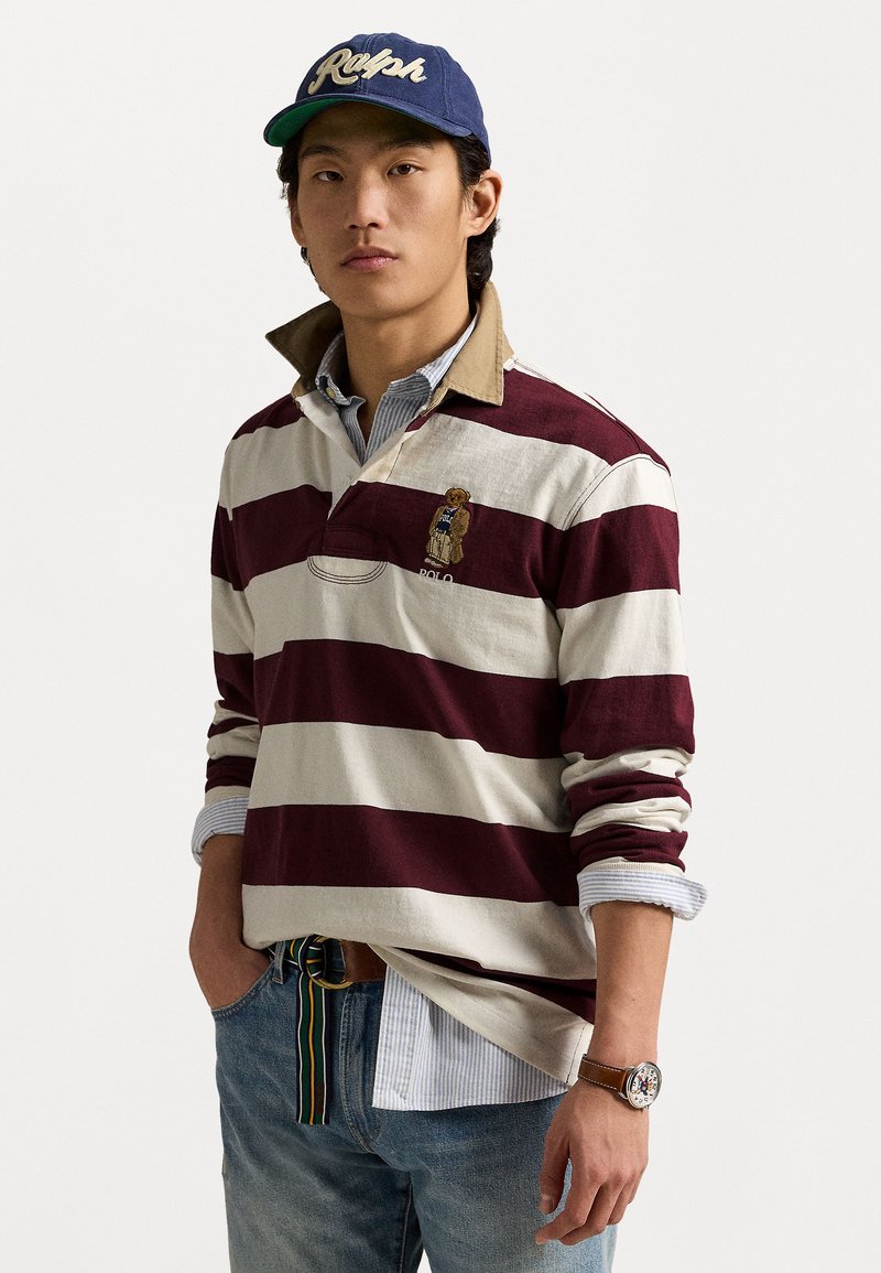Burgunder og hvitstripete langermet polo med brun krage og brodert bjørnelogo. Kombinert med denim og et brunt klokke.