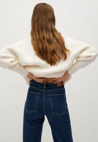 Biały prążkowany sweter z opuszczonymi ramionami, noszony z wysokim stanem ciemnoniebieskich dżinsów z czterema kieszeniami i brązowym paskiem ze skóry.