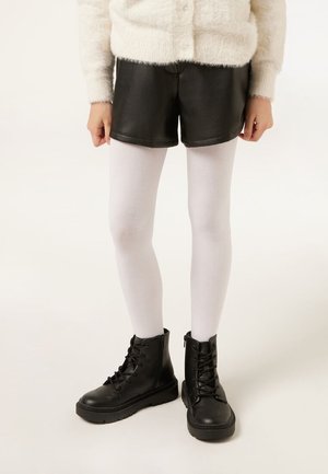 Child wearing white tights, black faux leather shorts, black combat boots, and a cream fuzzy sweater standing on a plain light background.