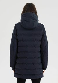 Granatowa kurtka puchowa z kapturem, z poziomymi pikowanymi panelami i nieco dłuższym tyłem. Gładka faktura i solidna konstrukcja.