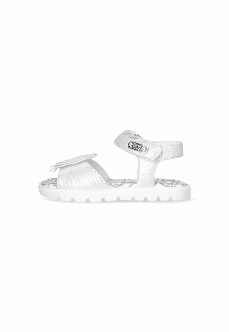 White synthetic sandals featuring a textured finish, adjustable strap with metallic hardware, and a decorative accent. Closed-toe design.