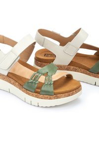 Sandalias de piel blanca con una correa de piel verde y detalle trenzado, media suela de corcho y suela exterior de goma ligera. Correa ajustable con cierre de Velcro.