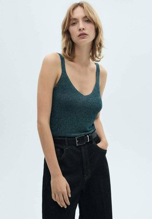 Top senza maniche color teal con scollatura a V profonda e una finitura luccicante, abbinato a jeans di denim scuri a vita alta e una cintura nera.