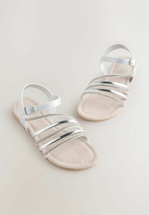 Sandales argentées à lanières avec semelle plate, ornées d'accents métalliques et scintillants, d'une semelle intérieure douce en velours et d'une sangle réglable à la cheville.