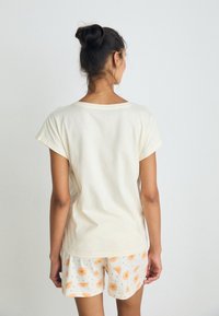 Light yellow cotton T-shirt with short sleeves, paired with white shorts featuring an orange and yellow fan pattern.
