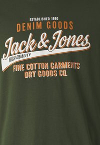 Dark green cotton t-shirt featuring white and orange text: "Jack & Jones," "DENIM GOODS," and "HIGH QUALITY," with established date 1990.