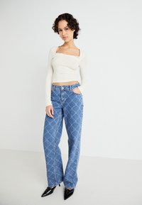 Cream ribbed long-sleeve top with square neckline; blue patterned wide-leg jeans; black pointed-toe heels; smooth textures; casual ensemble.