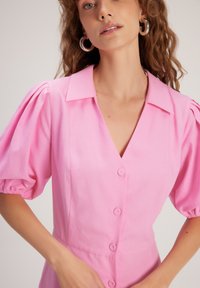 Abito rosa a maniche corte con scollatura a V, bottoni sul davanti e maniche a sbuffo. Tessuto liscio con vita aderente.