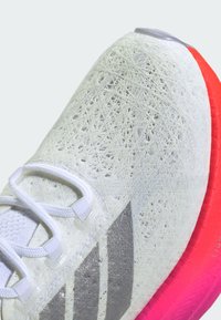 Scarpa da corsa bianca con tomaia in rete testurizzata, dettagli argento, lacci bianchi e una suola intermedia con una sfumatura da rosso a rosa. Presenta un design a tre righe.