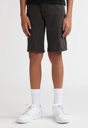 Donkergrijze denim shorts met een klassieke snit, kniehoogte en omgeslagen zoom, gecombineerd met witte sneakers en witte sokken die tot halverwege de kuit reiken.